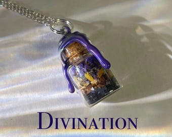 May include: A silver chain necklace with a glass bottle pendant filled with dried flowers and purple resin. The bottle is sealed with a cork stopper and has a purple resin drip running down the side. The text "DIVINATION" is printed below the bottle.