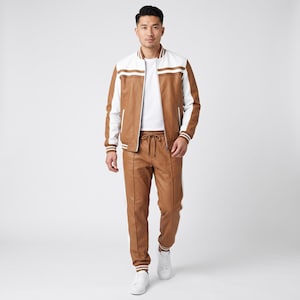 May include: A tan and white varsity-style jacket with a front zipper, paired with matching tan joggers featuring white side stripes and a drawstring waist, worn over a plain white t-shirt and finished with clean white sneakers.