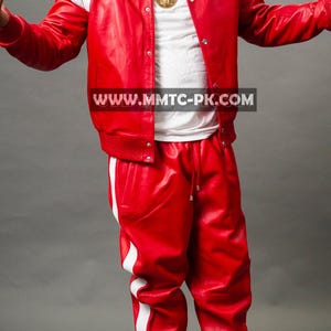 Pu&ograve; includere: Un completo in pelle rossa composto da un bomber con dettagli bianchi sulle spalle e pantaloni abbinati con strisce bianche laterali. L'outfit include una maglietta bianca e scarpe da ginnastica bianche. &Egrave; visibile anche una catena d'oro con un ciondolo.