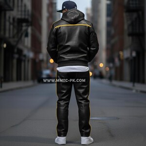 May include: Black leather jacket and pants set with yellow trim. The jacket has a hood and a white undershirt is visible. The pants have a matching yellow stripe down the side. The person is wearing a baseball cap and white sneakers.
