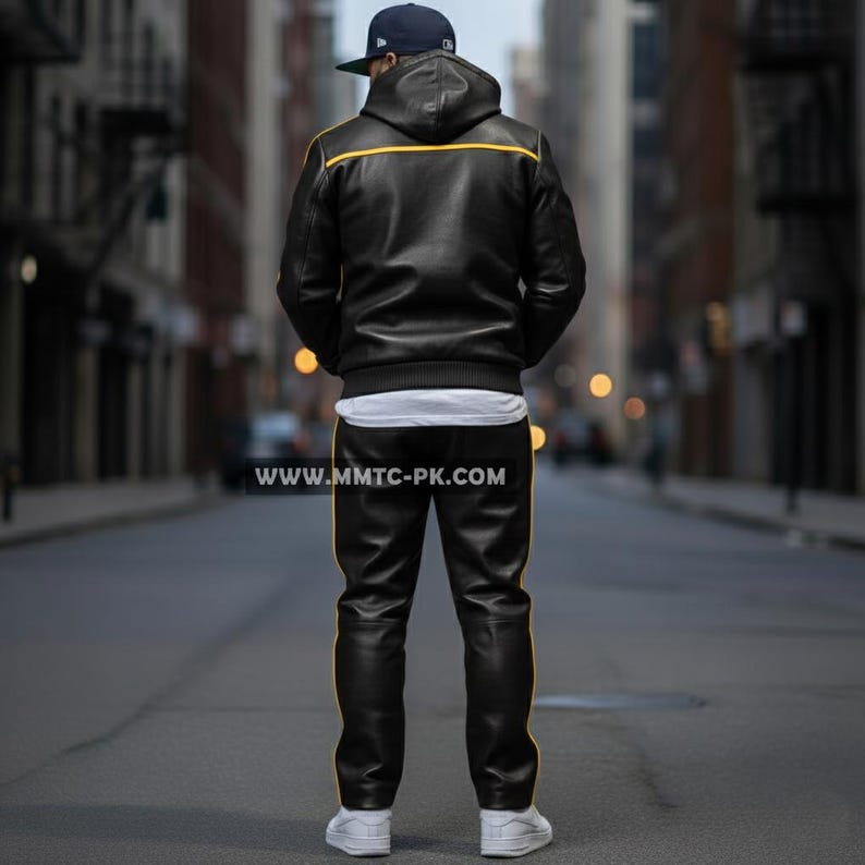 May include: Black leather jacket and pants set with yellow trim. The jacket has a hood and a white undershirt is visible. The pants have a matching yellow stripe down the side. The person is wearing a baseball cap and white sneakers.