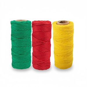 May include: Three spools of twine in vibrant colors: green, red, and yellow. Each spool is tightly wound and cylindrical, with a cardboard core visible at the top. The twine is likely made of a natural fiber.