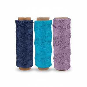 May include: Three spools of twine in shades of navy blue, turquoise, and lavender. Each spool is wrapped around a cardboard core. The twine is tightly wound, creating a textured appearance. Ideal for crafting and decorative projects.