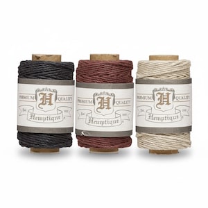 May include: Three spools of Hemptique twine in black, burgundy, and natural colors. Each spool has a paper label with the brand name and logo. The twine is wound around a cardboard core.
