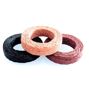 May include: Three spools of decorative twine in a close-up shot. The spools are circular and made of textured material. Colors include black, a light reddish-brown, and a darker burgundy. The spools are arranged on a white background.