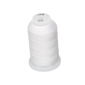 May include: A white spool of thread with the text "WHT" and "00" printed on the top. The thread is tightly wound around a white plastic base. The image is a close-up shot of the thread spool.