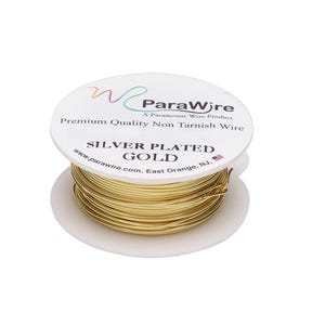 Puede incluir: Una bobina de alambre dorado chapado en plata con una etiqueta blanca que dice ParaWire, Premium Quality Non Tarnish Wire, SILVER PLATED GOLD y la dirección del sitio web. El alambre está enrollado en una bobina de plástico blanco con una bandera.