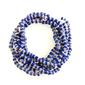 Può includere: Una lunga fila di piccole perline di vetro a forma di barilotto disposte in una spirale circolare. Ogni perlina presenta un colore di base blu intenso con strisce bianche verticali e sottili linee arancioni incassate tra i segmenti.