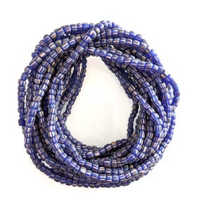 Può includere: Una disposizione circolare di molteplici fili di piccole perline rotonde. Ogni perlina presenta un colore di base blu intenso con sottili strisce verticali bianche che corrono lungo la circonferenza, creando un motivo uniforme.