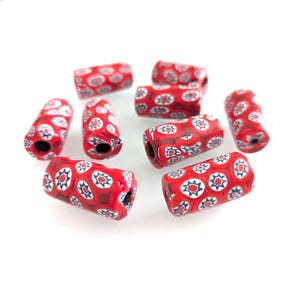May include: A collection of red, cylindrical glass beads with a floral pattern in white, blue, and red. The beads are approximately 0.5 inches long and have a hole running through the center, suitable for stringing into jewelry.
