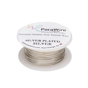 Peut inclure: Une bobine de fil argenté avec une étiquette blanche portant l'inscription ParaWire, A Paramount Wire Product, Premium Quality Non Tarnish Wire, SILVER PLATED SILVER et l'adresse du site web. Le fil est enroulé sur une bobine en plastique blanc.