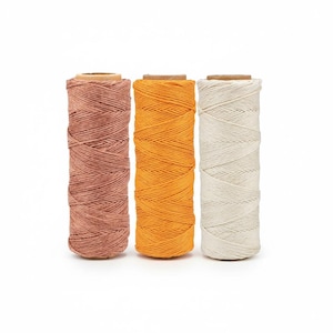 May include: Three spools of twine in pink, orange, and white. The twine is tightly wound around a cardboard core. The spools are arranged vertically against a white background, showcasing the texture and colour variations.
