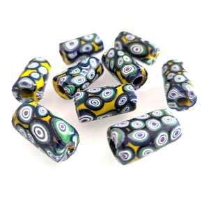 Pode incluir: Uma coleção de contas de vidro cilíndricas com base amarela e um padrão de círculos concêntricos em tons de azul, verde e branco. As contas estão espalhadas sobre uma superfície branca, mostrando seu design único e variações de cor.