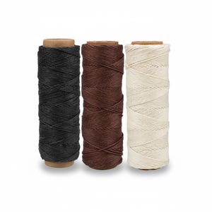 May include: Three spools of waxed thread in black, brown, and off-white. The thread is tightly wound around cardboard cores, showcasing the texture and color variations. Ideal for crafting and leatherwork projects.