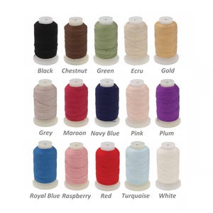 Puede incluir: Una colección de carretes de hilo en varios colores, incluyendo negro, castaño, verde, crudo y dorado. Colores adicionales son gris, granate, azul marino, rosa, ciruela, azul real, frambuesa, rojo, turquesa y blanco. Cada carrete está etiquetado con su nombre de color.