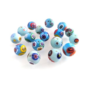 Pode incluir: Uma coleção de contas de vidro redondas em vários tons de azul, adornadas com padrões florais e geométricos coloridos. As contas estão espalhadas, mostrando seus intrincados desenhos e texturas. Estas contas são ideais para fazer joias e projetos de artesanato.