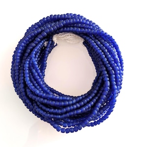 May include: A circular arrangement of small, matte cobalt blue glass beads strung together on a white thread. The beads are uniform in size and shape, creating a continuous loop of deep blue color that contrasts with the white string visible at the top.