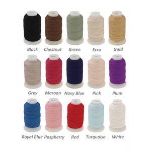 Könnte beinhalten: Eine Sammlung von Garnrollen in verschiedenen Farben, darunter Schwarz, Kastanie, Grün, Ecru und Gold. Weitere Farben sind Grau, Bordeaux, Marineblau, Rosa und Pflaume. Das Bild zeigt auch Garnrollen in Royalblau, Himbeere, Rot, Türkis und Weiß. Jede Rolle ist mit ihrem Farbnamen beschriftet.