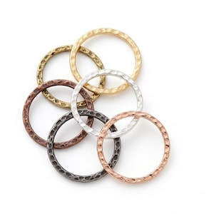 May include: A collection of six circular metal rings featuring a hammered, textured surface. The rings are finished in various metallic tones, including gold, silver, copper, bronze, and dark gunmetal, arranged in an overlapping cluster.
