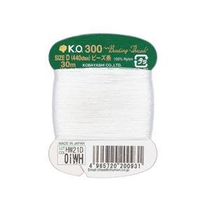 Pode incluir: Um carretel de fio branco para miçangas com uma etiqueta verde e branca. A etiqueta diz "K.O. 300 Beading Thread" e "SIZE D". O carretel contém 30 metros de fio 100% nylon. A etiqueta também inclui um código de barras e o texto "MADE IN JAPAN".