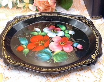 May include: Black oval serving tray with a floral design. The tray features a black background with hand-painted flowers in red, pink, and white, with green leaves. The rim is edged with a gold decorative trim.