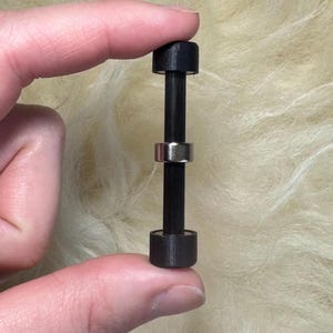 May include: A small black dumbbell with a silver ring in the middle.