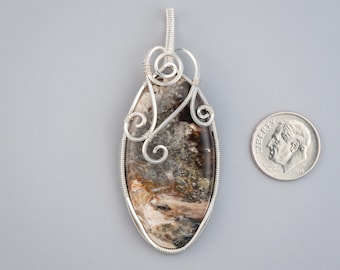 May include: A silver wire wrapped pendant featuring a brown and white agate stone. The pendant is oval shaped and has a delicate wire design.