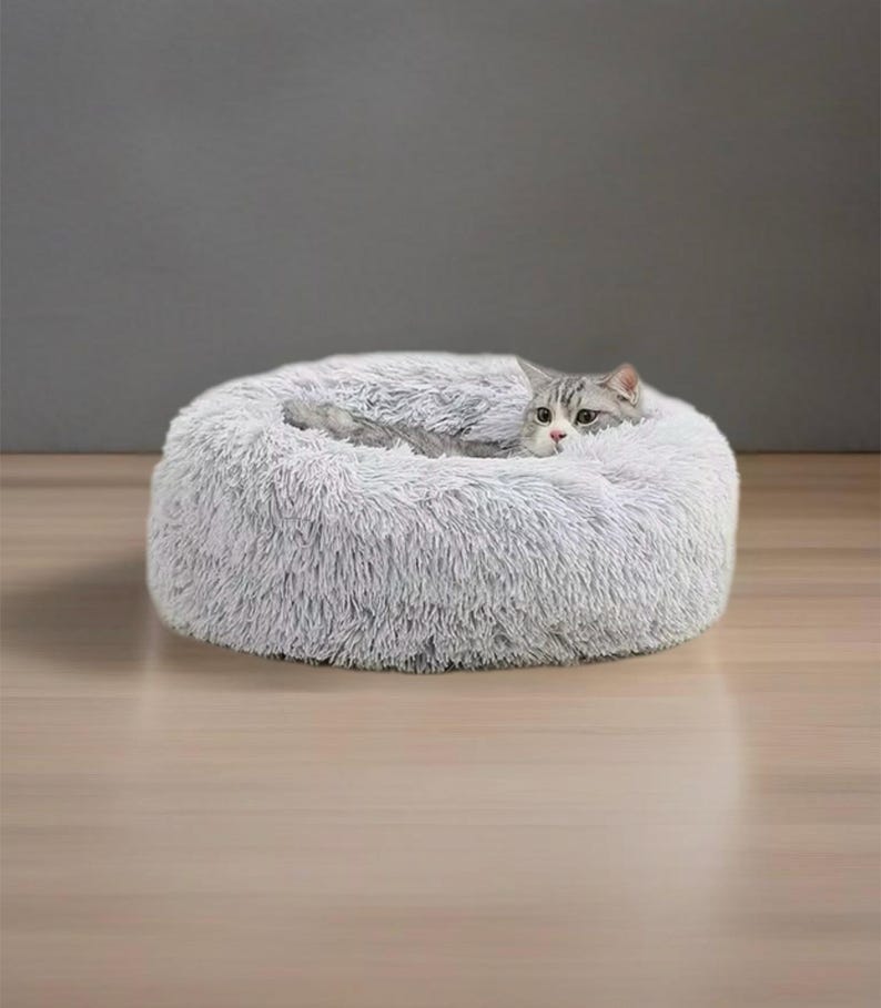 May include: A gray fluffy pet bed with a cat curled up inside. The bed is round and has a raised edge.