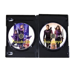 May include: Two-disc DVD set of the Marvel series "Hawkeye" featuring a black case with a front cover image of the main characters, Clint Barton and Kate Bishop, in their purple costumes. The text "Hawkeye" is visible on the discs.