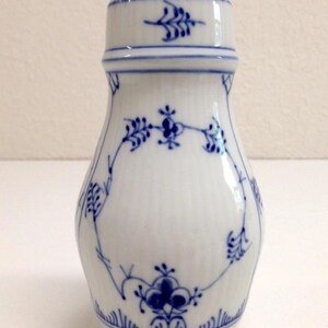 May include: A white porcelain salt shaker with a blue floral pattern. The shaker has a small, round lid with holes for sprinkling salt.
