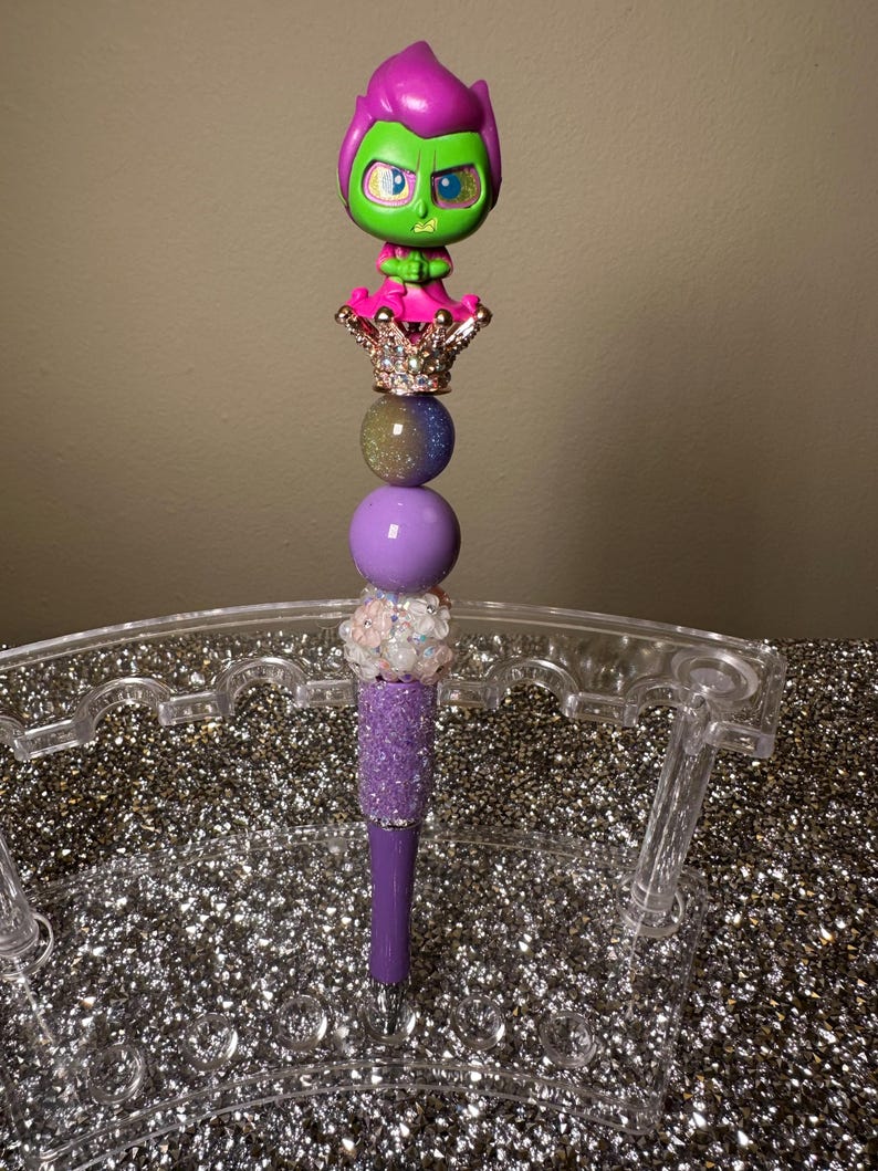 May include: Purple and green pen with a glittery purple body and a crown topped with a green and pink character figurine.