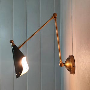 May include: A gold-toned wall-mounted light fixture with a black and white cone-shaped shade. The light is on and illuminating the room.