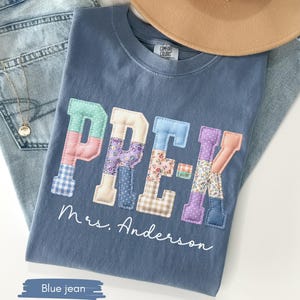 May include: A blue Comfort Colors t-shirt with the word "PREK" in patchwork letters. The letters are in various colors and patterns. The name "Mrs. Anderson" is written below the letters. A tan hat and blue jeans are in the background.