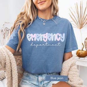 May include: Blue jean t-shirt with the words "emergency department" in a playful font. The word "emergency" is in pink and blue, with a floral pattern. The word "department" is in a script font.