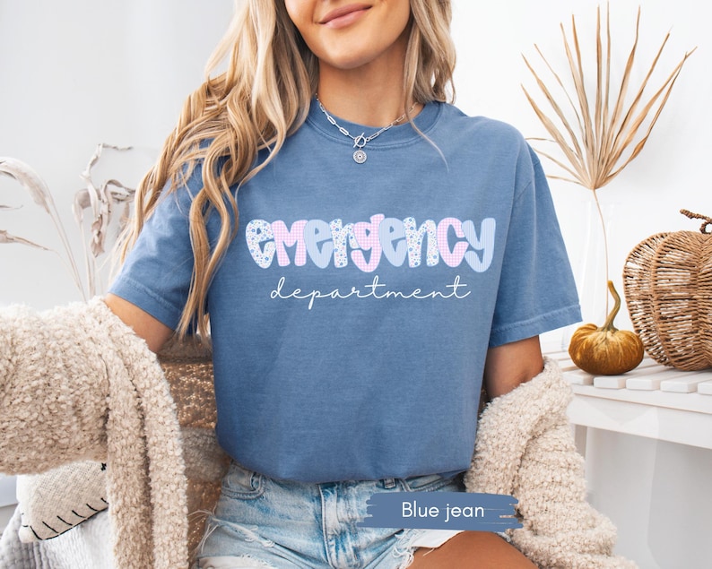 May include: Blue jean t-shirt with the words "emergency department" in a playful font. The word "emergency" is in pink and blue, with a floral pattern. The word "department" is in a script font.