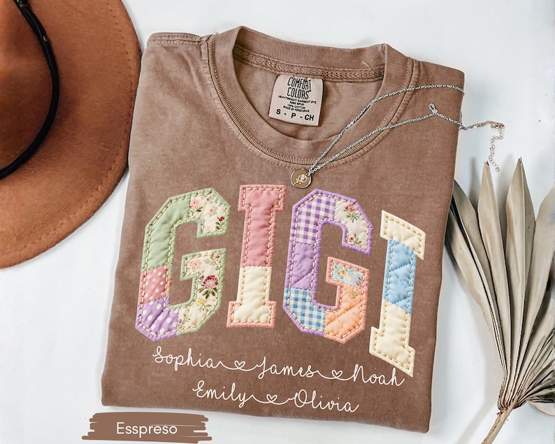 May include: Espresso-colored t-shirt with the word "GIGI" in patchwork letters. The letters are in various pastel colors and floral patterns. Below the word are names: Sophia, James, Noah, Emily, and Olivia.
