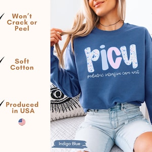 May include: Indigo blue sweatshirt with the word "PICU" in a floral and gingham pattern. The text "pediatric intensive care unit" is below the word. The sweatshirt is made of soft cotton and produced in the USA.