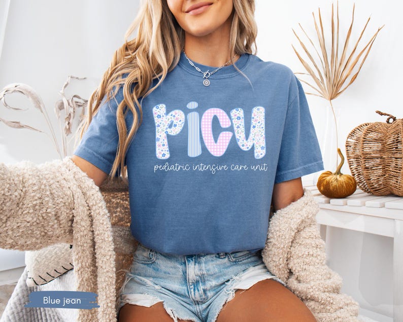 Puede incluir: Camiseta azul vaquero con las letras "PICU" en un dise&ntilde;o floral, a rayas y a cuadros. Las palabras "pediatric intensive care unit" est&aacute;n impresas debajo. La camiseta est&aacute; hecha de un material suave.