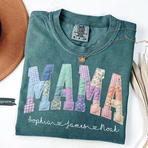 Puede incluir: Una camiseta Comfort Colors verde azulado con la palabra "MAMA" en letras de patchwork. Las letras est&aacute;n hechas de varias telas estampadas. Debajo de la palabra "MAMA" est&aacute;n los nombres "Sophia", "James" y "Noah". Tambi&eacute;n se ven un collar dorado y un sombrero marr&oacute;n.