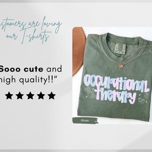 Op de afbeelding: Mosgroen t-shirt met de woorden "Occupational Therapy" in een kleurrijk, speels lettertype. Het shirt heeft ook kleine grafische elementen en een gouden ketting. De afbeelding bevat de tekst "Sooo cute and high quality!!".