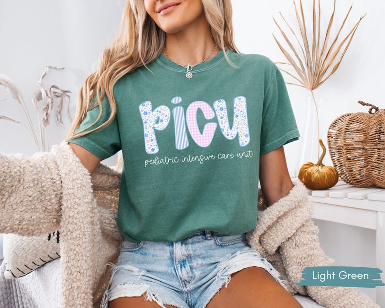Puede incluir: Camiseta verde claro con las letras "PICU" en un dise&ntilde;o floral, a rayas y de cuadros. Las palabras "pediatric intensive care unit" est&aacute;n impresas debajo. La camiseta es de manga corta y cuello redondo.