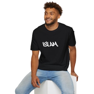 May include: Black t-shirt with the word "ISLAM" in white, stylized lettering. The shirt is a crew neck and is being worn by a person. The person is wearing blue jeans and is sitting down.