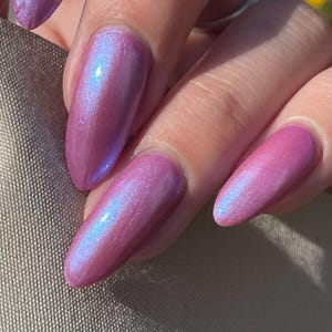 May include: Close-up of a hand with several nails painted in a shimmery pink nail polish with a blue iridescent sheen.