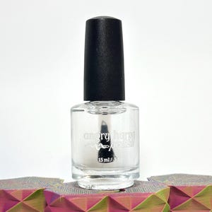 May include: Clear nail polish bottle with a black cap. The bottle has the words "angry happy polish" printed on it. The bottle contains 15 ml / 0.5 fl oz of polish. The bottle is sitting on a colorful geometric surface.