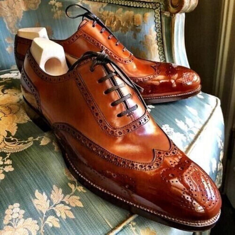 May include: Brown leather oxford shoes with a wingtip design and a polished finish. The shoes have a lace-up closure and a decorative pattern on the toe.