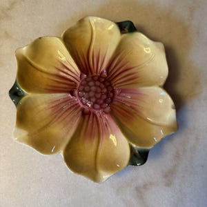 May include: A ceramic flower-shaped dish featuring a glossy finish with cream-colored petals that transition into a deep pink center. The edges of the petals show subtle dark green shading, and the surface displays a fine, visible crackle glaze pattern.