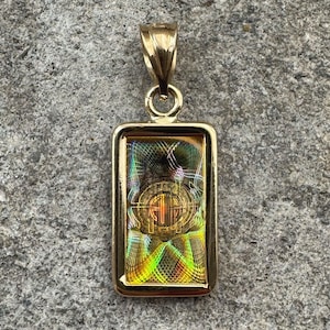 May include: A gold pendant necklace with a rectangular charm featuring a colorful, abstract design. The charm has a gold frame and a shimmering, iridescent finish.
