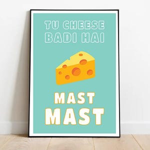 May include: A framed art print with a teal background and a yellow cheese wedge illustration. The text reads "TU CHEESE BADI HAI" above the cheese and "MAST MAST" below. The print is in a black frame.