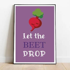 May include: A framed art print with a purple background and a red beet illustration with green leaves. The text "Let the BEET DROP" is written in white, stylized font.