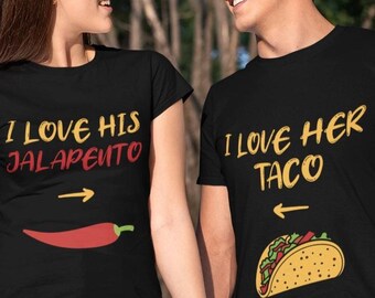 May include: A couple wearing matching black t-shirts with a food-themed design. The woman's shirt says "I love his jalapeno" with a red chili pepper and an arrow pointing to the right. The man's shirt says "I love her taco" with a yellow taco and an arrow pointing to the left.